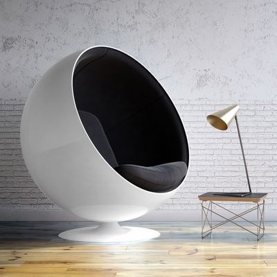  Eero Aarnio - Chaise Ball noire et blanche dans une pièce avec un parquet en bois et un fond gris. A droite de la chaise se trouve une table basse avec une lampe posée dessus.